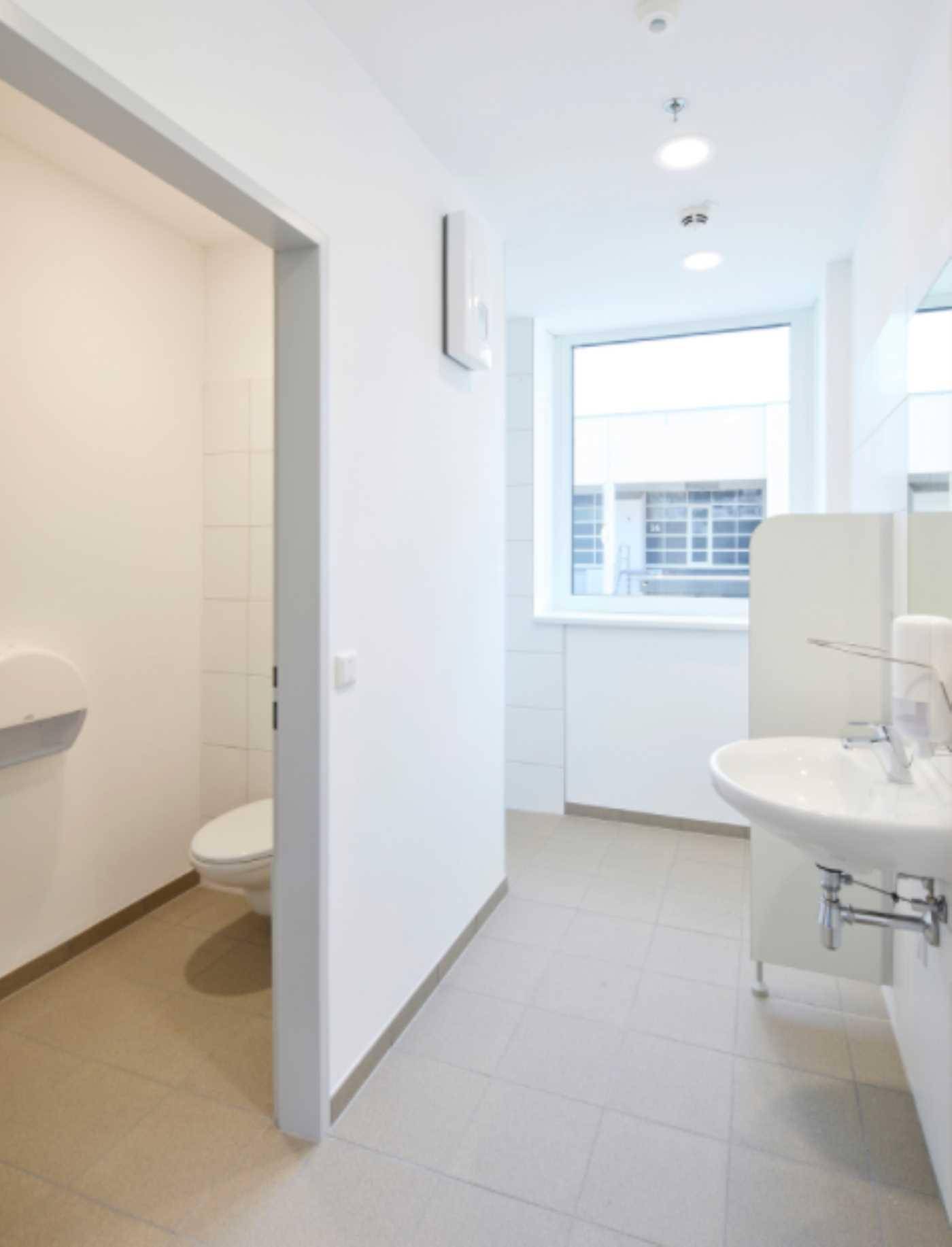 Heller Sanitärbereich mit Waschbecken, Toilette und Fenster, ausgestattet mit weißen Fliesen.