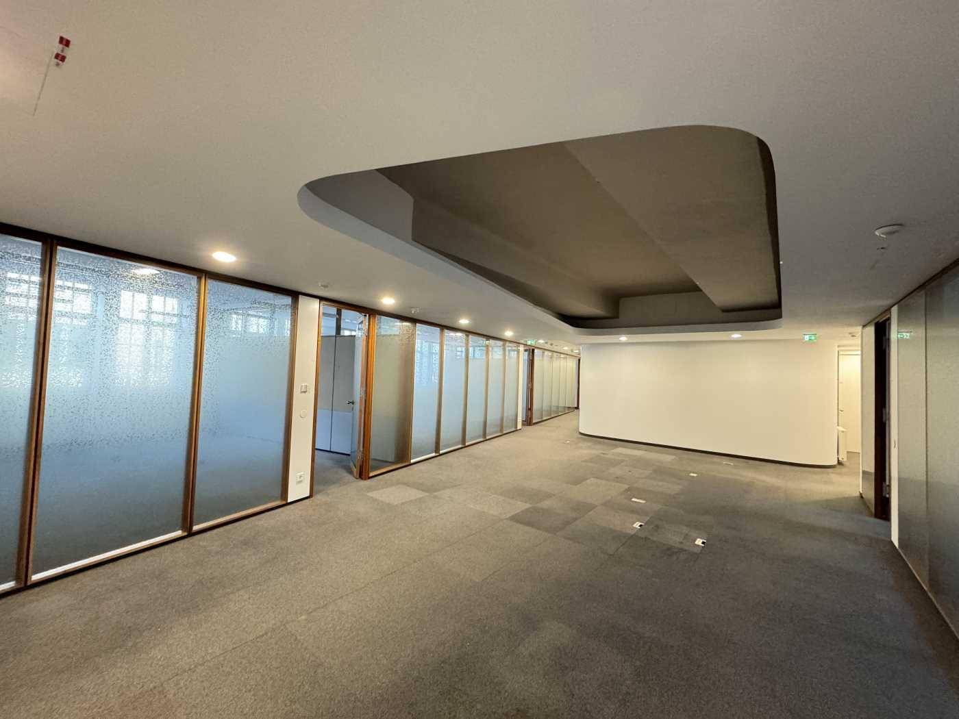 Moderner Bürobereich mit Teppichboden, Glaswänden und einer stilvollen Deckenaussparung.