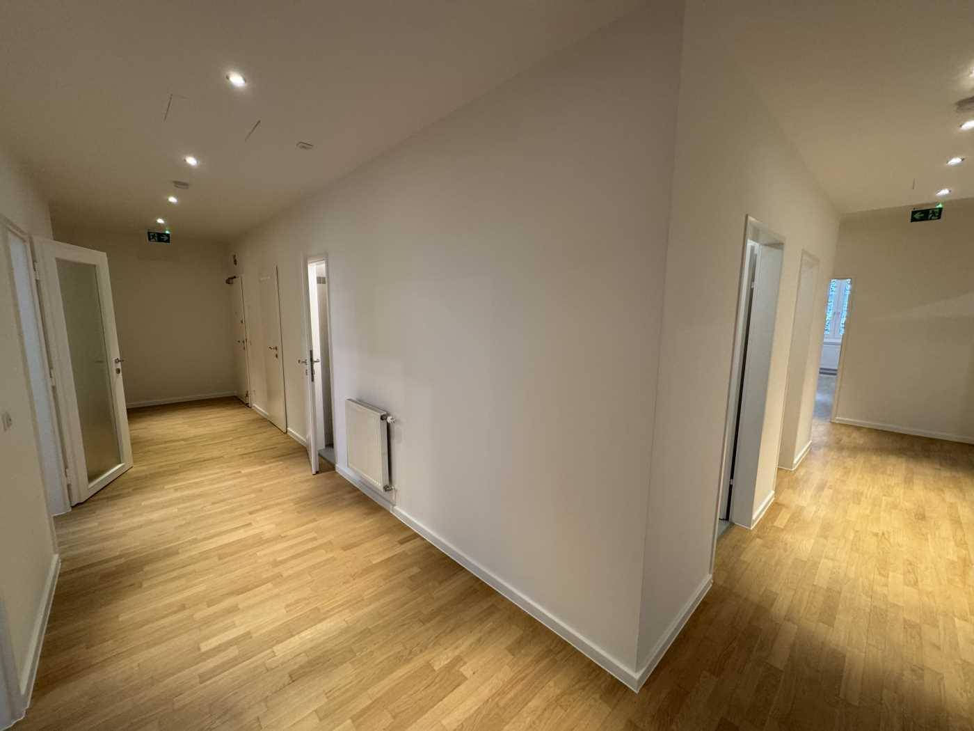 Langer, heller Flur mit Holzboden und mehreren Türen, beleuchtet durch Einbaustrahler.