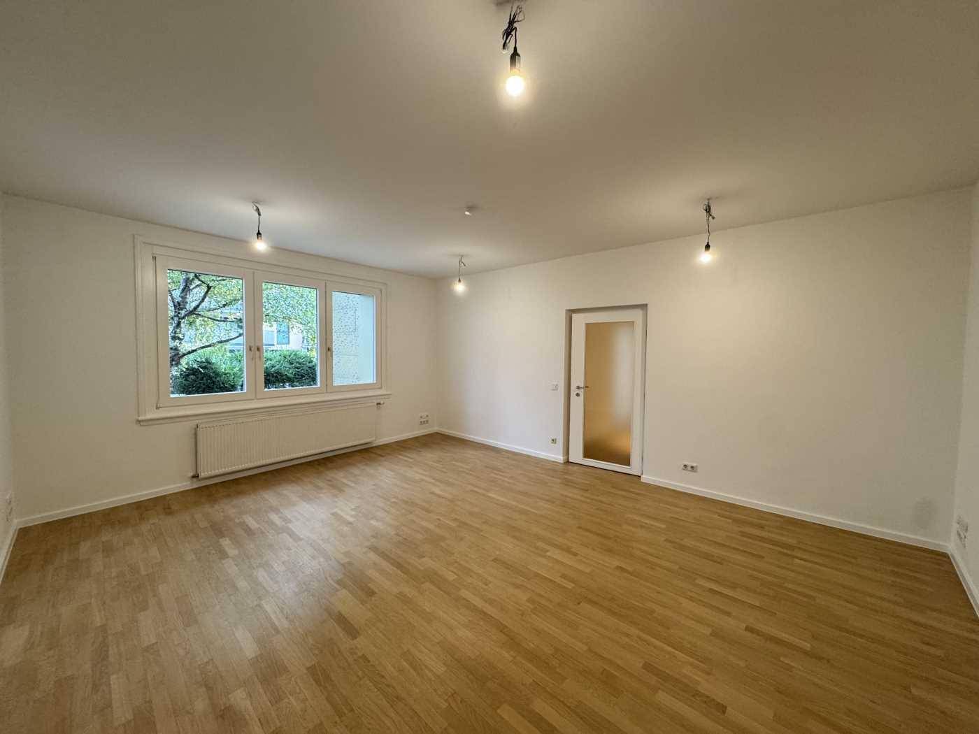 Heller Büroraum mit Holzboden und einem großen Fenster, das den Blick ins Grüne freigibt.