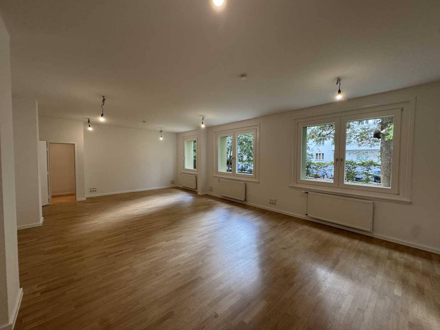 Großer, heller Büroraum mit Holzboden und mehreren Fenstern, die viel Tageslicht hereinlassen.