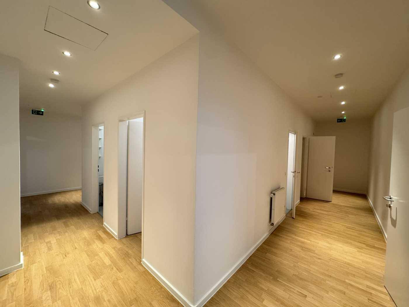Heller Flur mit Holzboden und mehreren Türen, beleuchtet durch Einbaustrahler in der Decke.