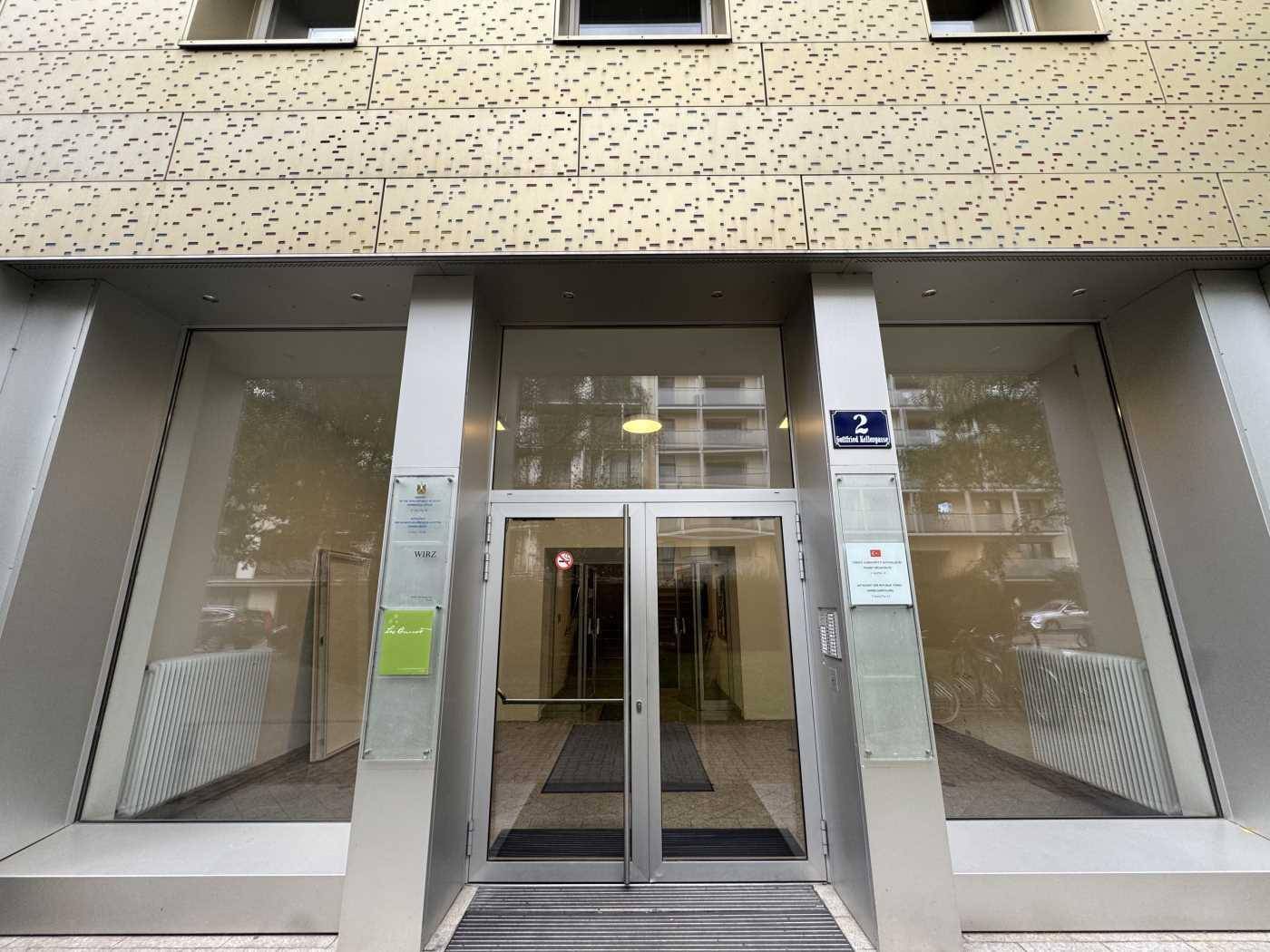 Moderner Gebäudeeingang mit großen Glastüren und einer strukturierten Fassade.