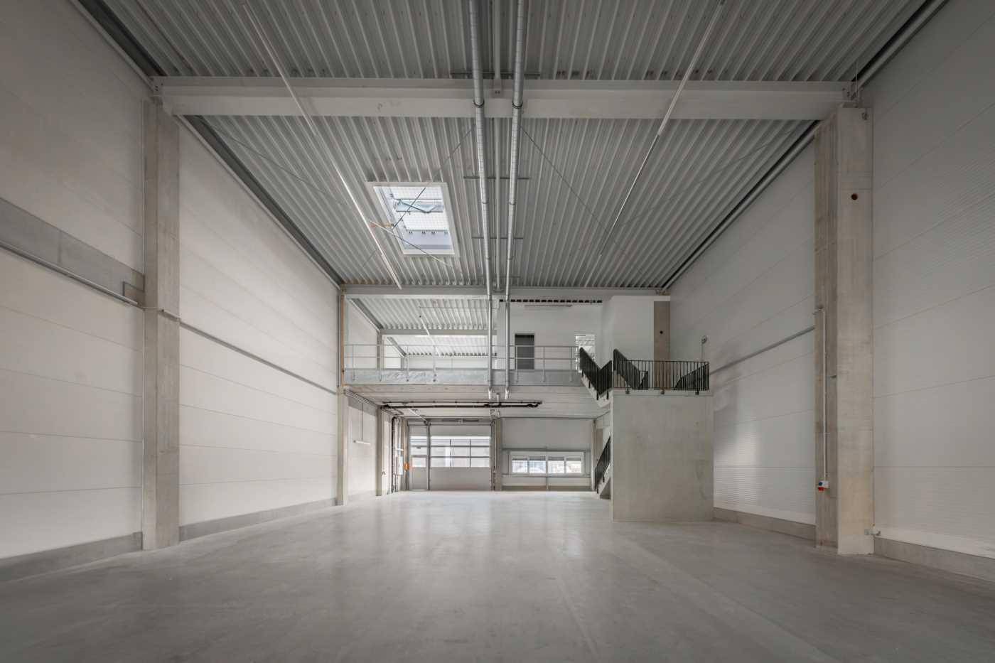 Weitläufiger, leerer Industrieraum mit sehr hoher Decke, sichtbaren Trägern und einer Mezzanine-Ebene.