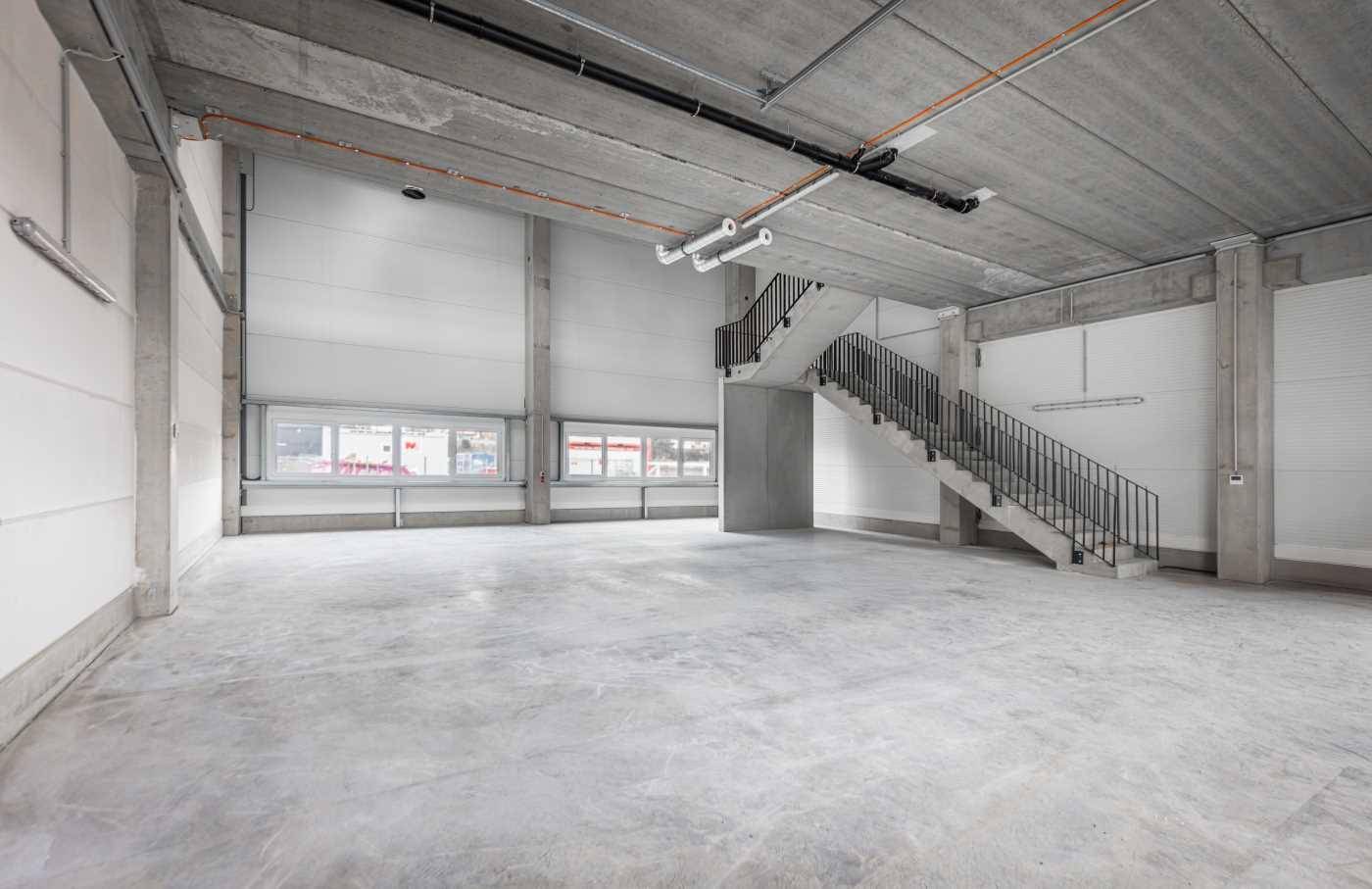 Geräumige Lagerhalle mit Betonboden, hohen Decken und einer freistehenden Betontreppe.