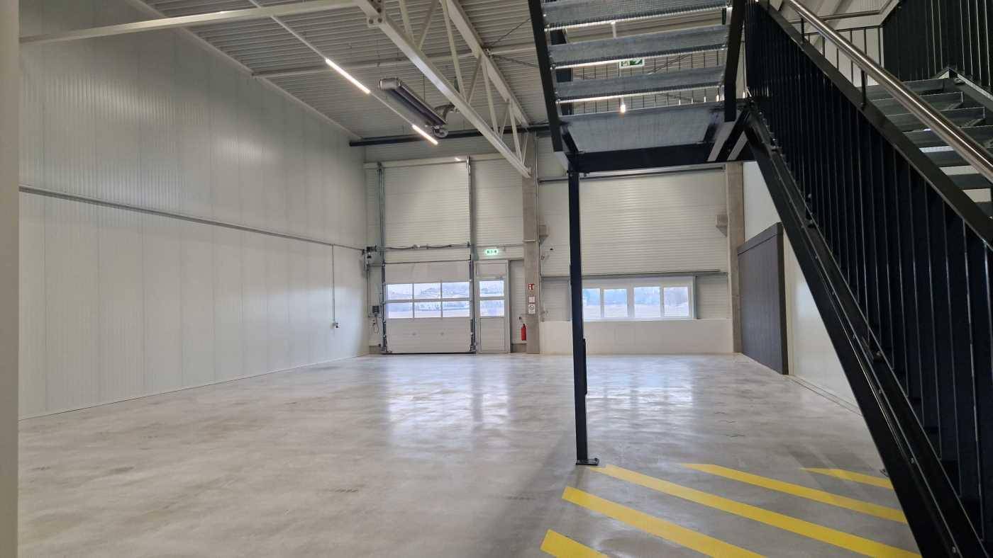 Moderner Industrieraum mit Betonboden, hohen Decken und einem Rolltor, das Tageslicht hereinlässt.
