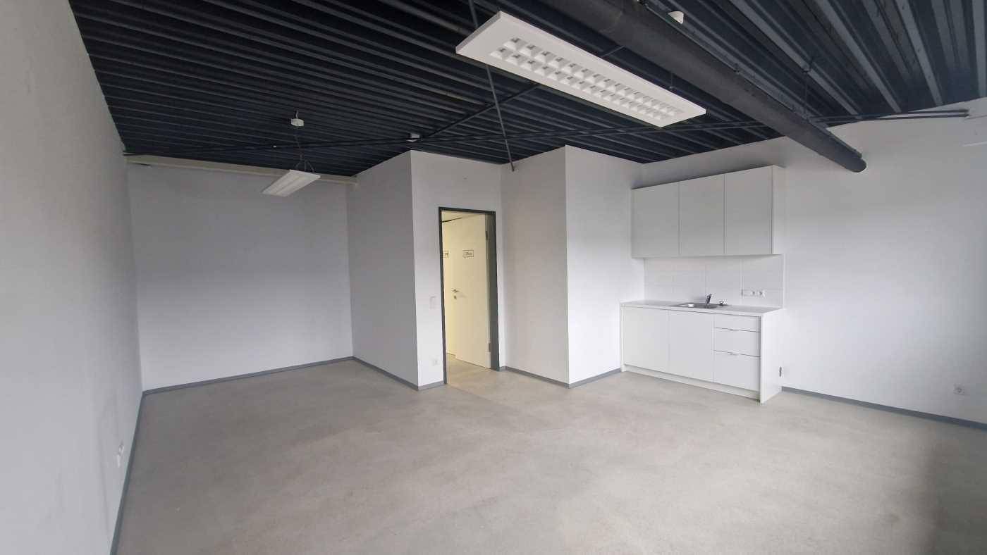 Kleiner Büroraum mit integrierter Küchenzeile, Betonboden und dunkler Deckenverkleidung.