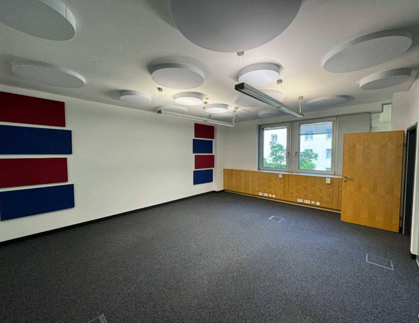 Büro mit Teppichboden, schallabsorbierenden Deckenplatten und farbigen Wandpaneelen für verbesserte Akustik.