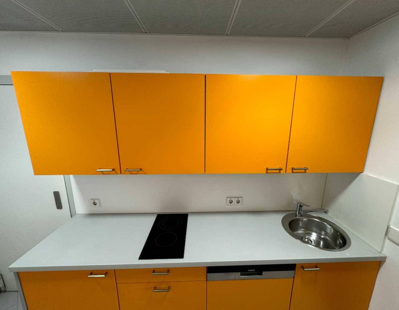 Kleine, moderne Küchenzeile mit leuchtend orangefarbenen Schränken, Spüle und Kochfeld.