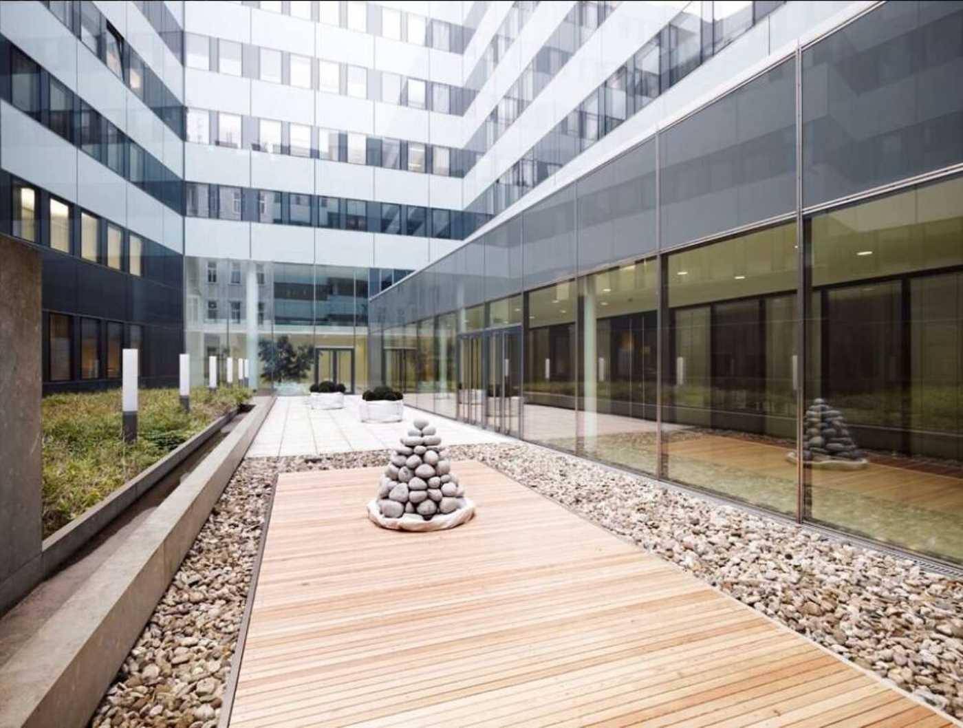 Moderner Innenhof mit Holzterrasse, Kiesbeeten und Glasfassaden des umliegenden Gebäudes.