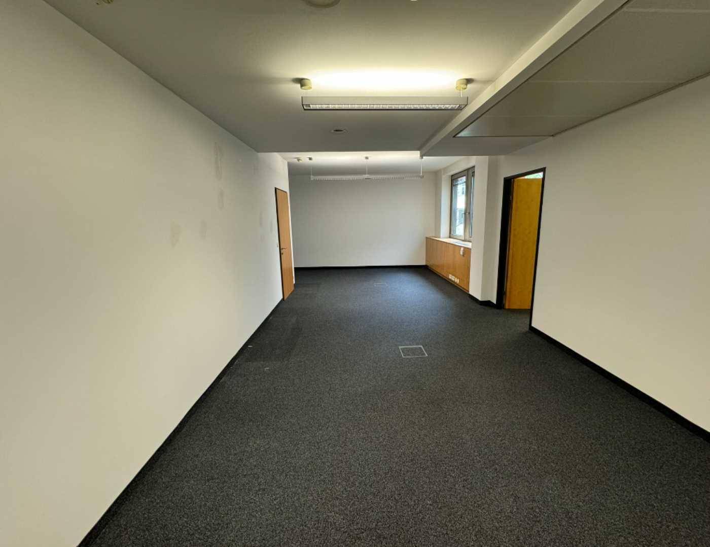 Leerer Büroraum mit Teppichboden und mehreren Türen, bereit für die individuelle Gestaltung.