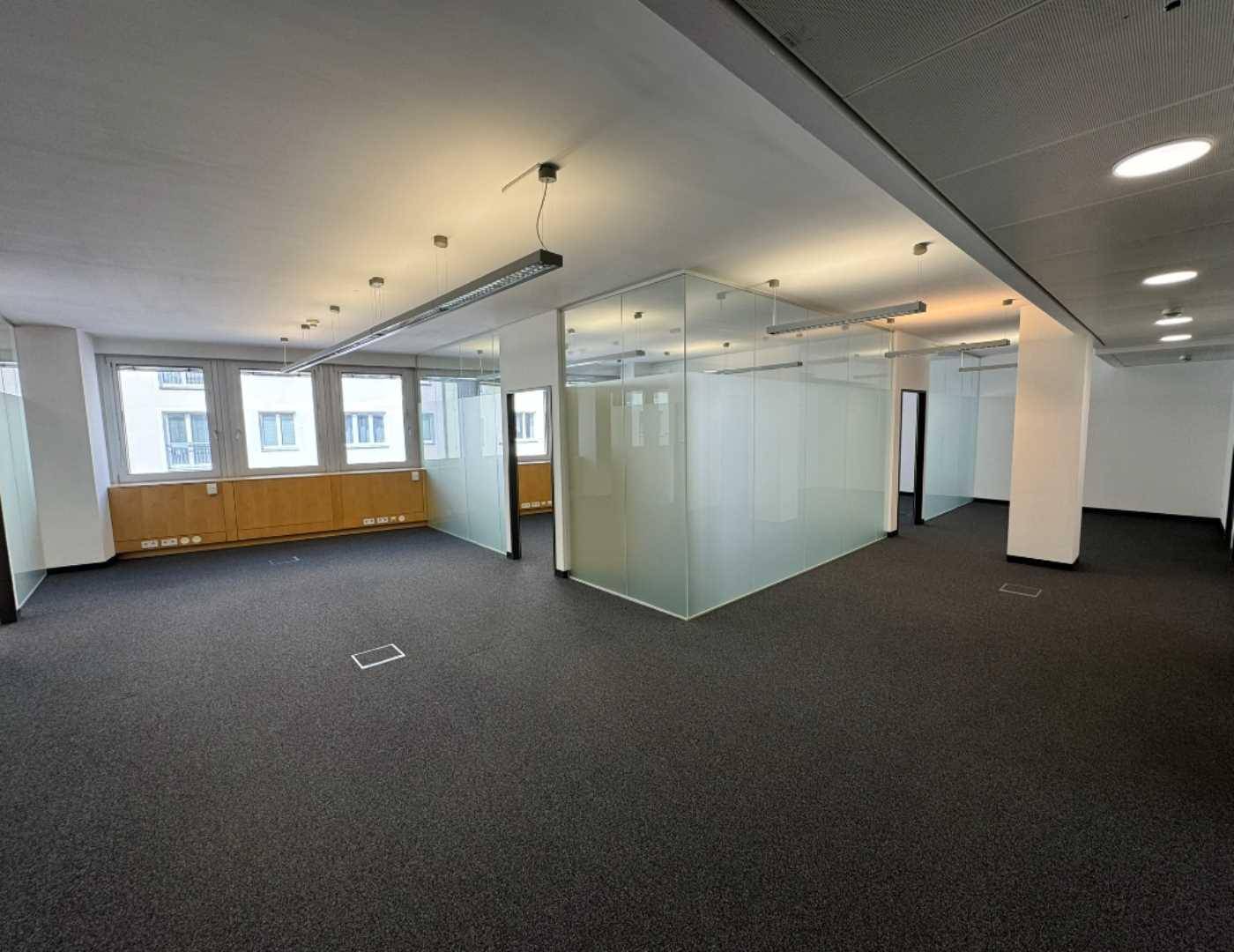 Großes Büro mit Teppichboden, flexiblen Glasabtrennungen und Fenstern, die viel Tageslicht hereinlassen.