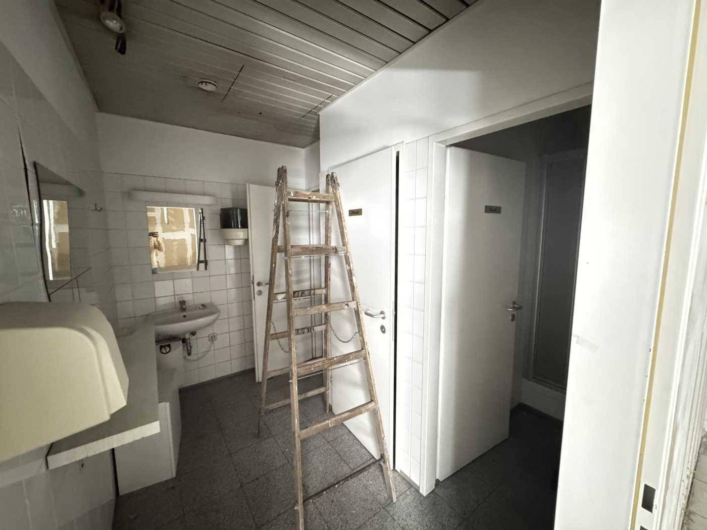 Funktionales Badezimmer mit Waschbecken und weißen Fliesen, inklusive einer Leiter für Wartungsarbeiten.