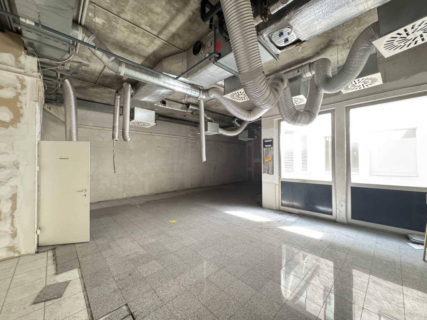Geräumiger Gewerberaum mit freiliegenden Lüftungssystemen und Fliesenboden, ideal für Umbau.
