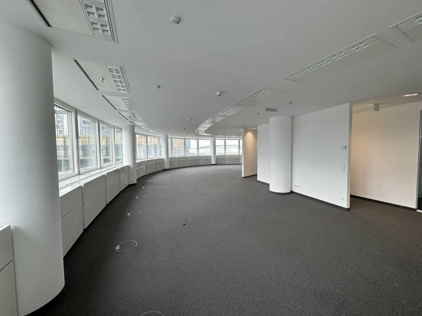 Weiter Bürobereich mit Teppichboden, gebogener Fensterfront und Blick auf die Umgebung.