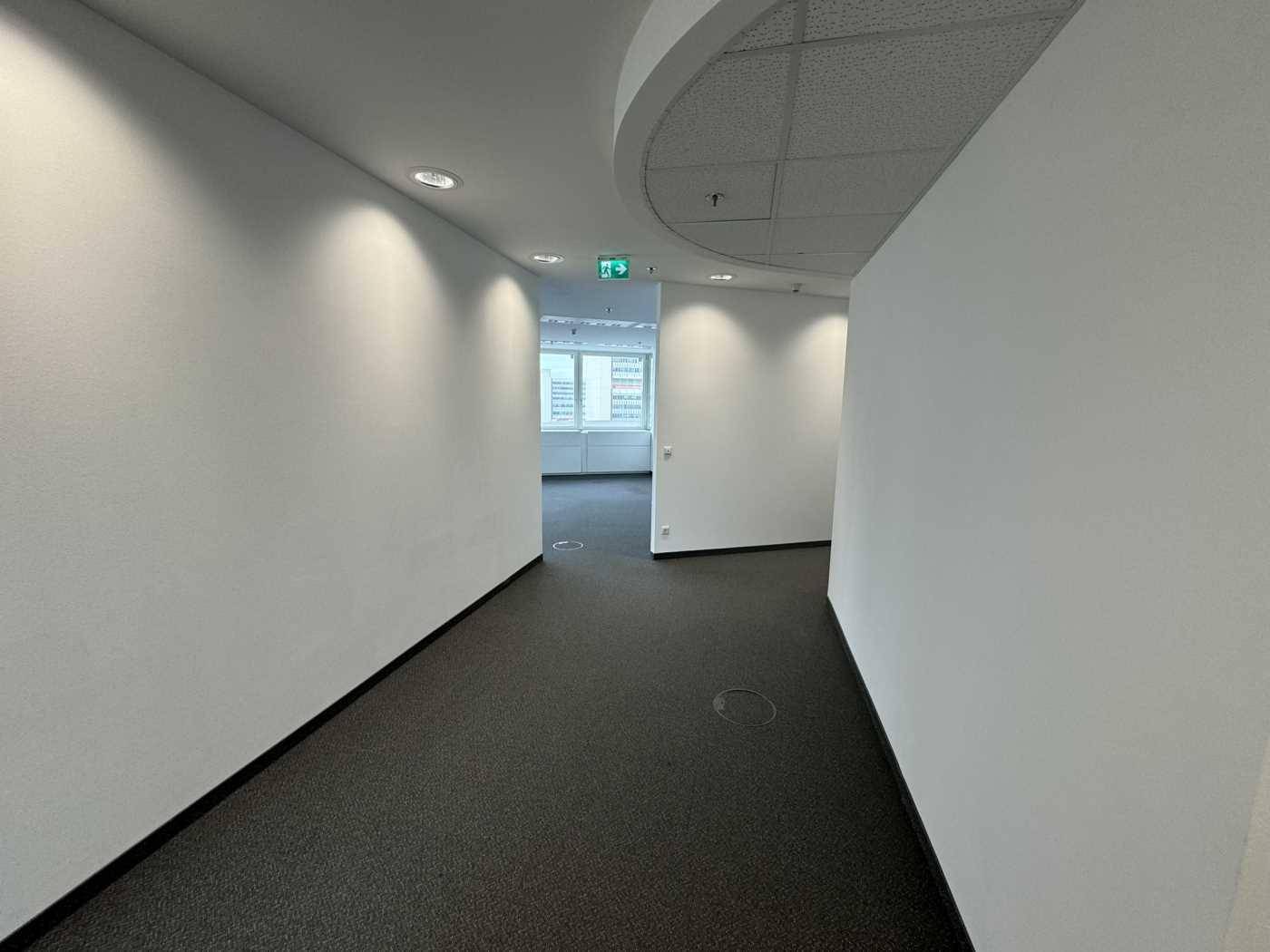 Moderner Flur mit Teppichboden und weißen Wänden, der zu verschiedenen Büroräumen führt.