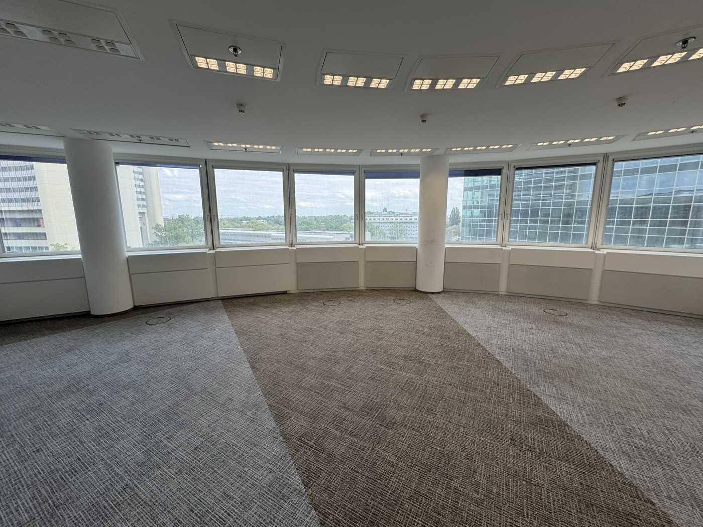 Runder Büroraum mit Teppichboden und einer beeindruckenden Fensterfront, die einen Panoramablick bietet.