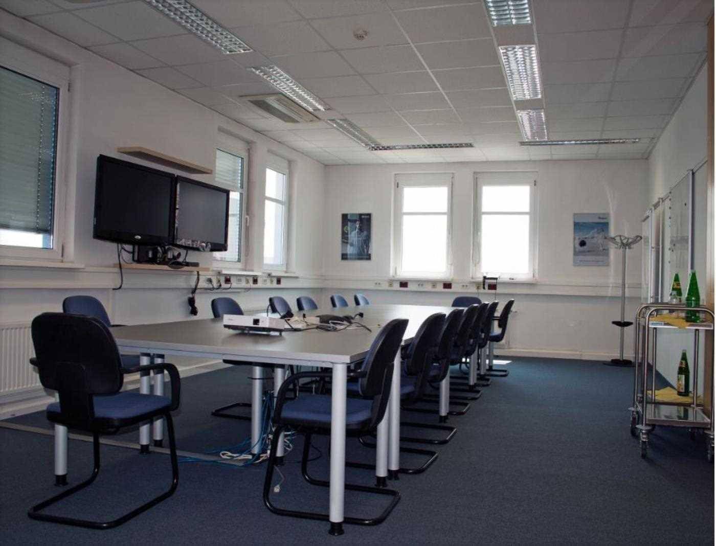 Geräumiger Konferenzraum mit langem Tisch, vielen Stühlen und Wandbildschirmen für Präsentationen.