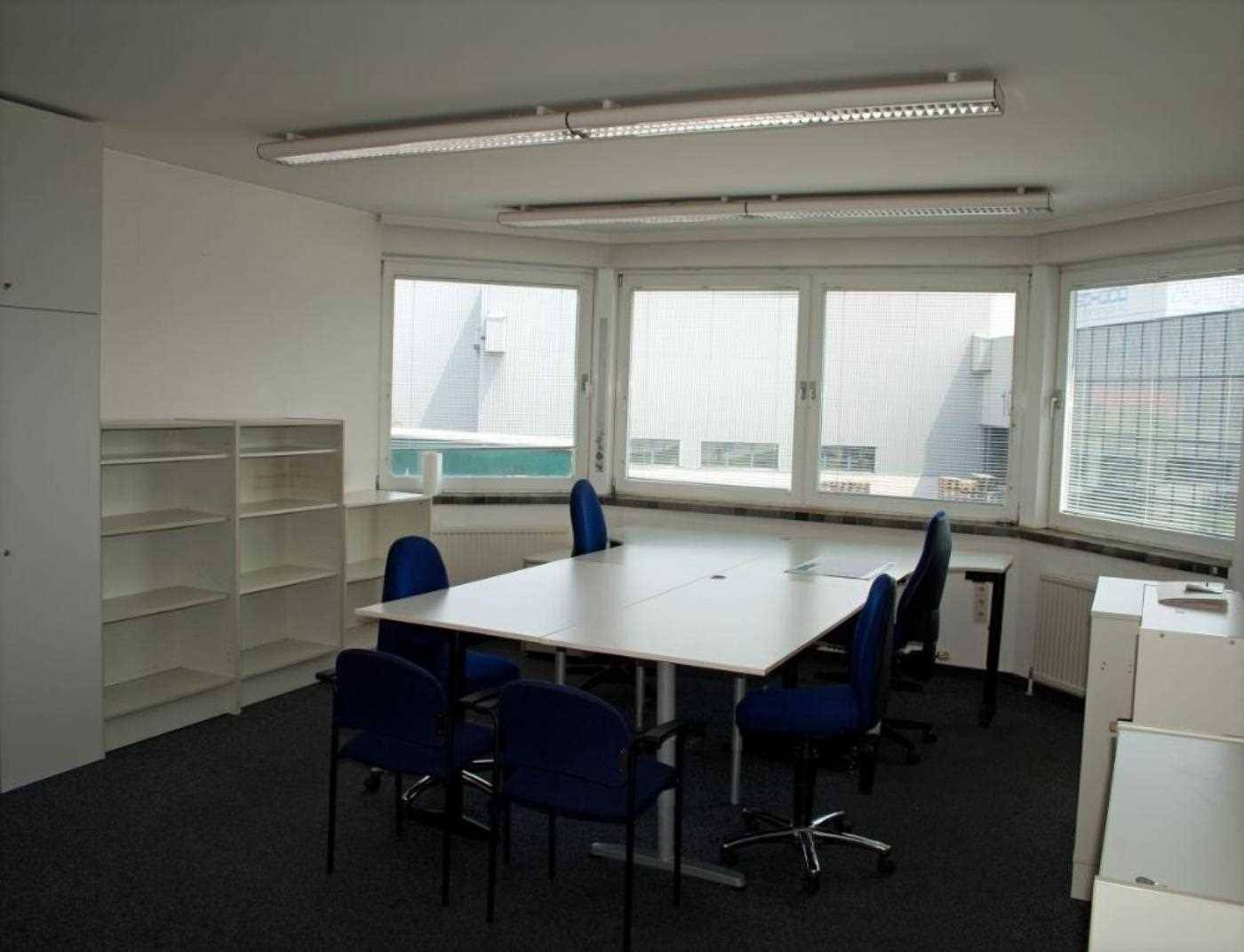 Heller Konferenzraum mit großem Tisch, blauen Stühlen und vielen Fenstern für natürliches Licht.