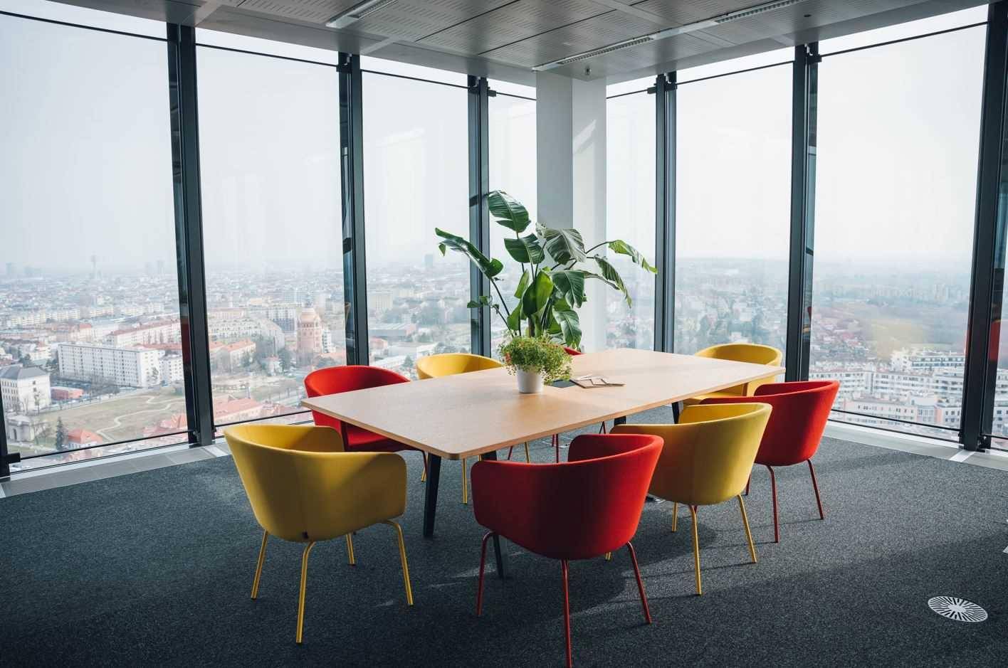 Heller Konferenzraum mit großen Fenstern, bunten Stühlen und Panoramablick über die Stadtlandschaft.