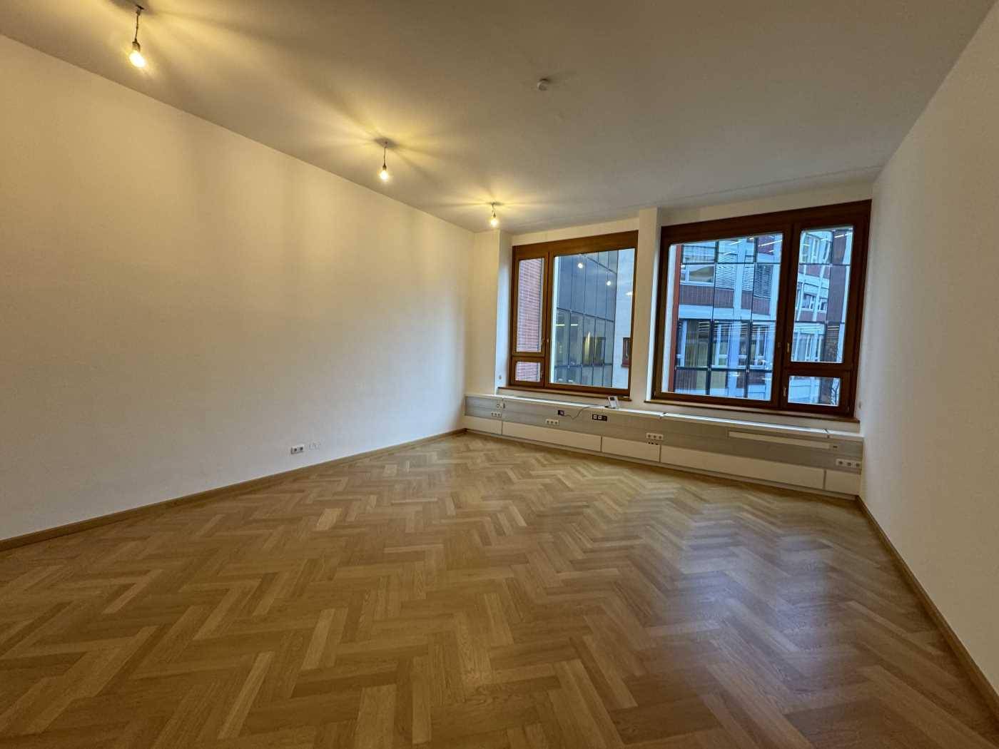 Heller Wohnraum mit Fischgrätparkett und großen Fenstern, die viel Tageslicht hereinlassen.