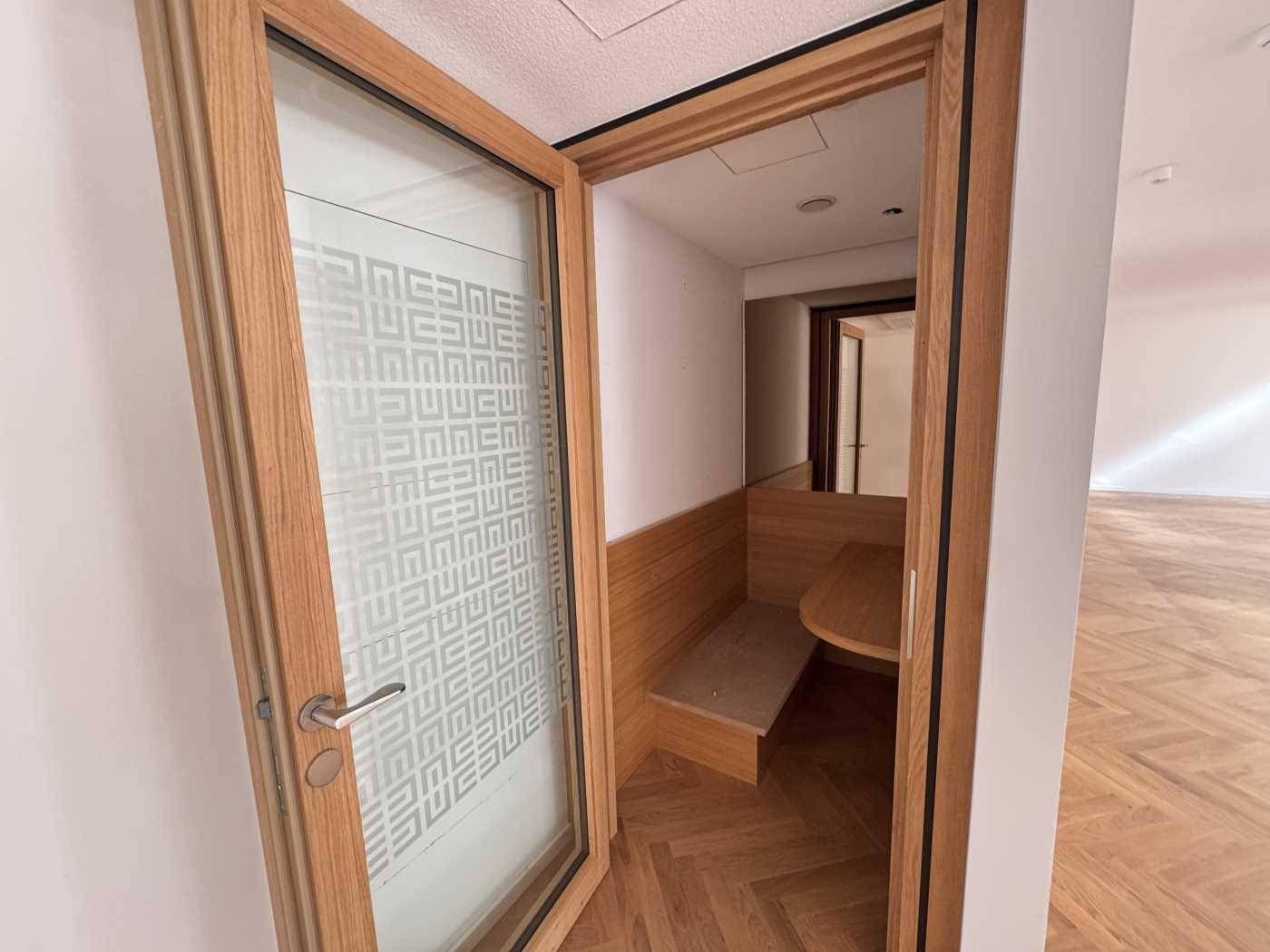 Kleiner, privater Arbeitsbereich mit Holztisch und Sitzbank, abgetrennt durch eine Glastür im Büro.