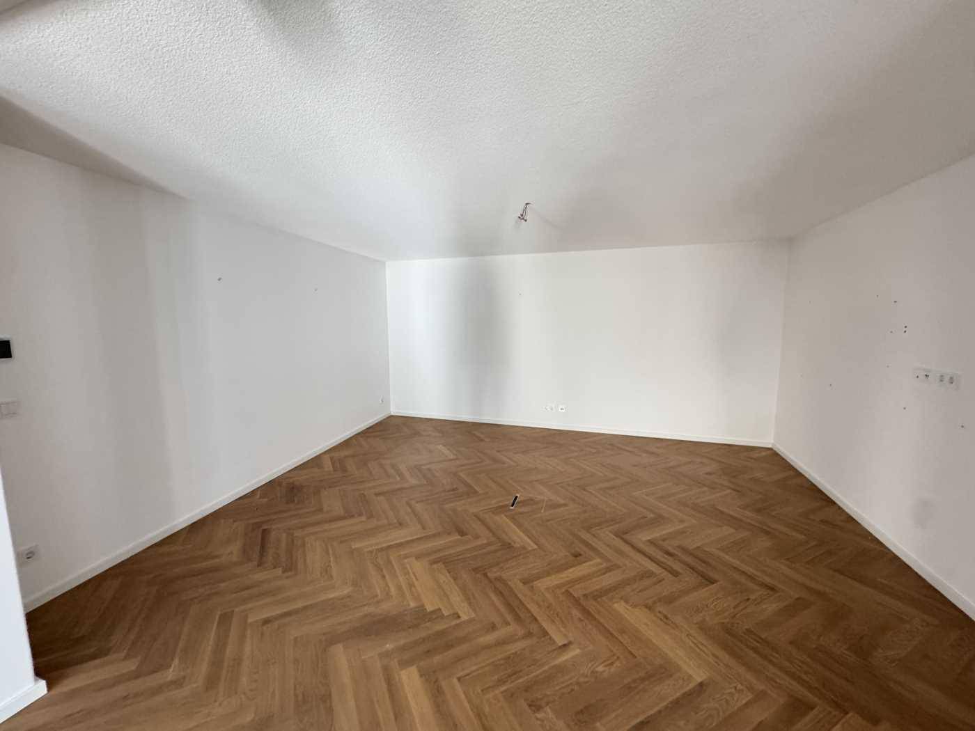 Leerer, heller Raum mit Fischgrätparkett und weißen Wänden, bereit für neue Einrichtungskonzepte.