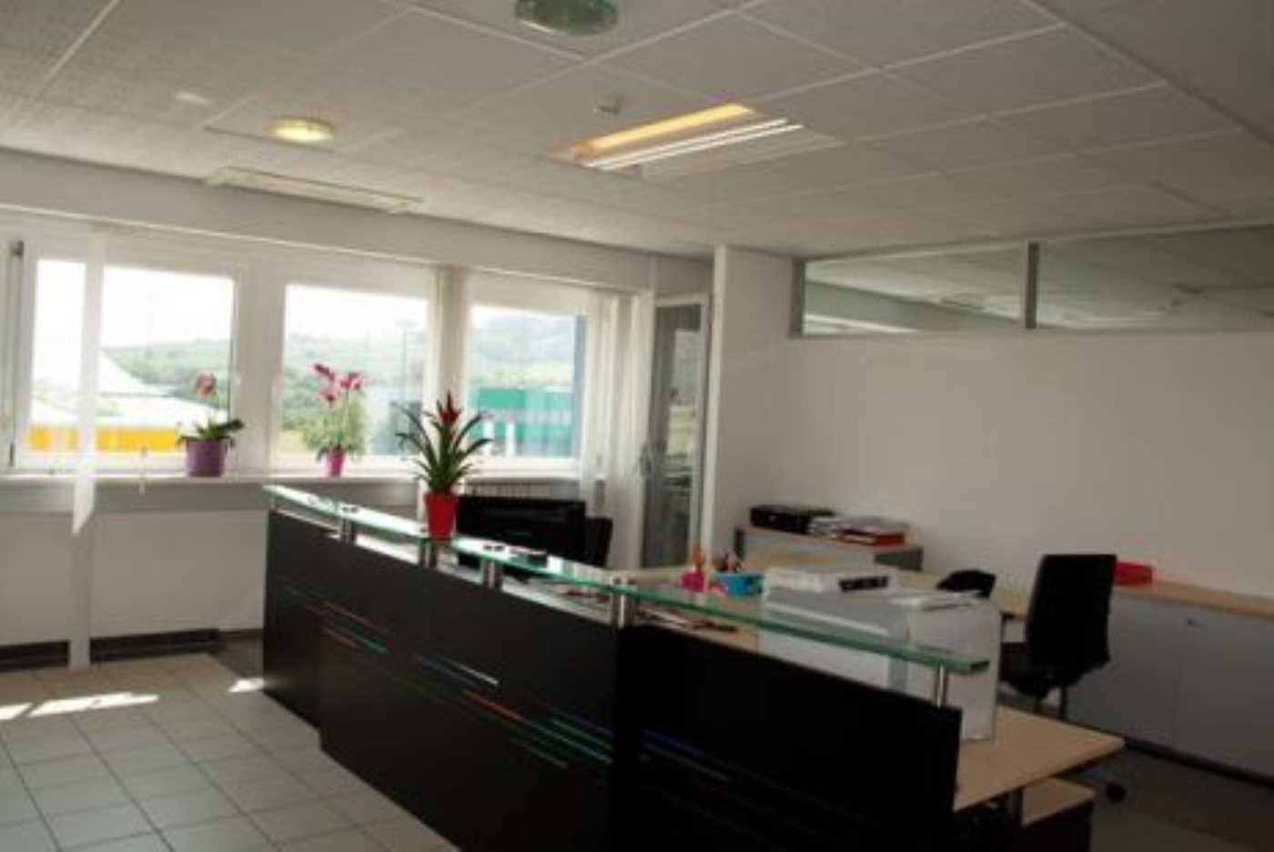 Empfangsbereich mit dunklem Tresen, Fliesenboden und großen Fenstern mit viel Tageslicht.