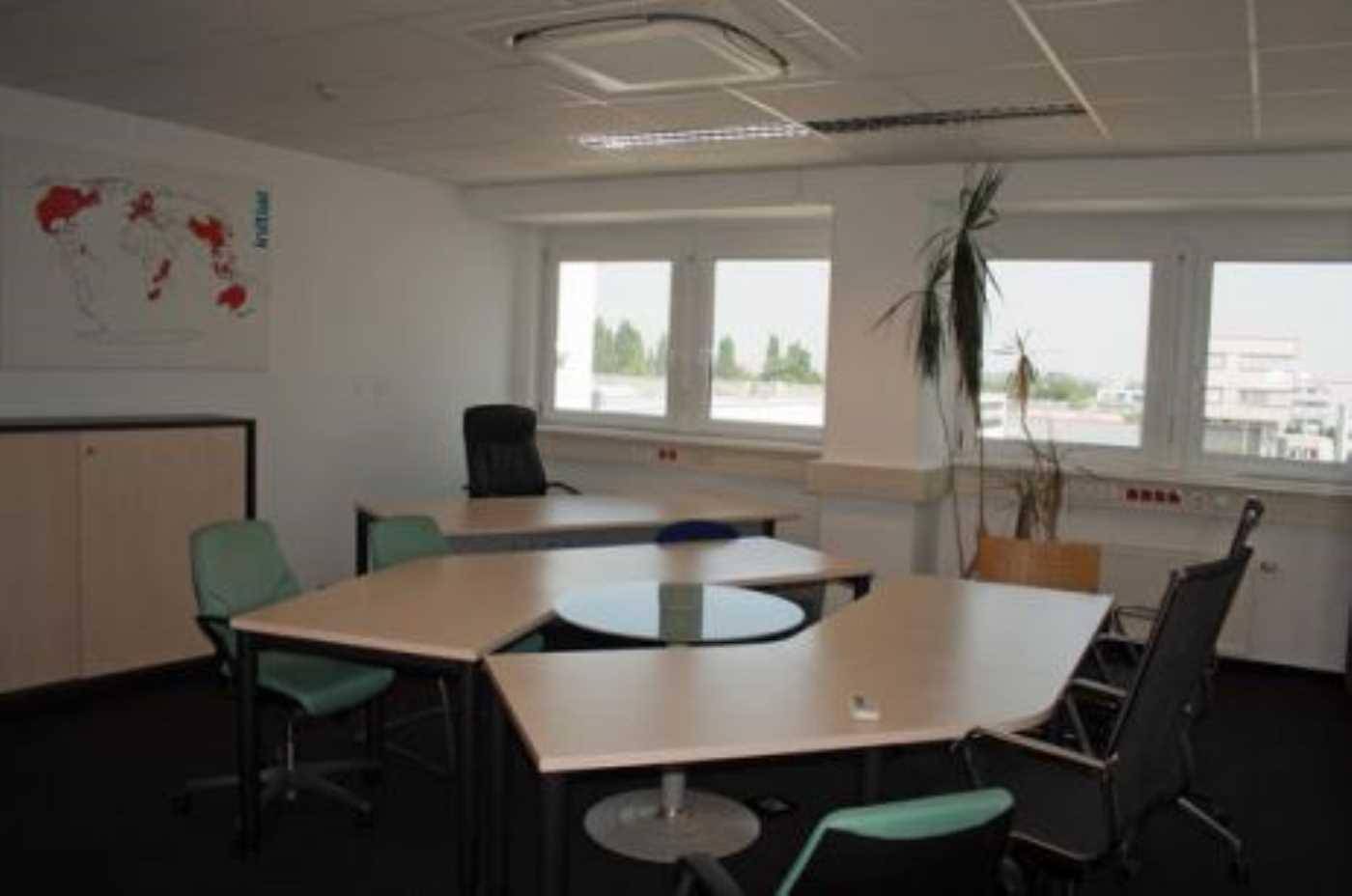 Geräumiges Büro mit mehreren Schreibtischen, Teppichboden und großen Fenstern.