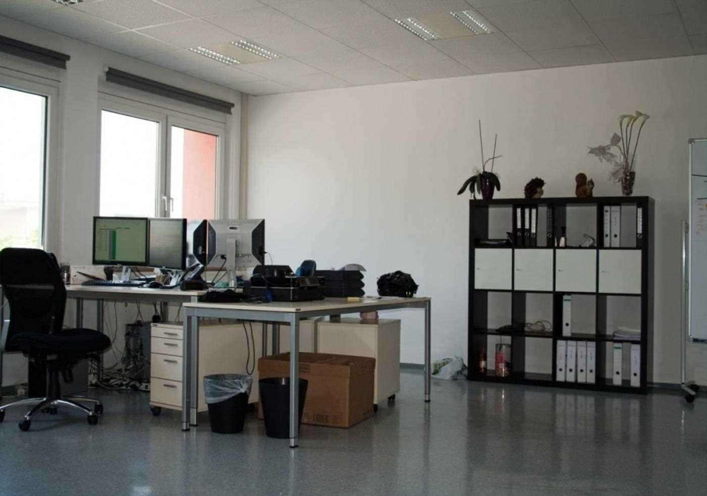 Modern eingerichtetes Büro mit Computern, Regalen und großen Fenstern für viel Tageslicht.