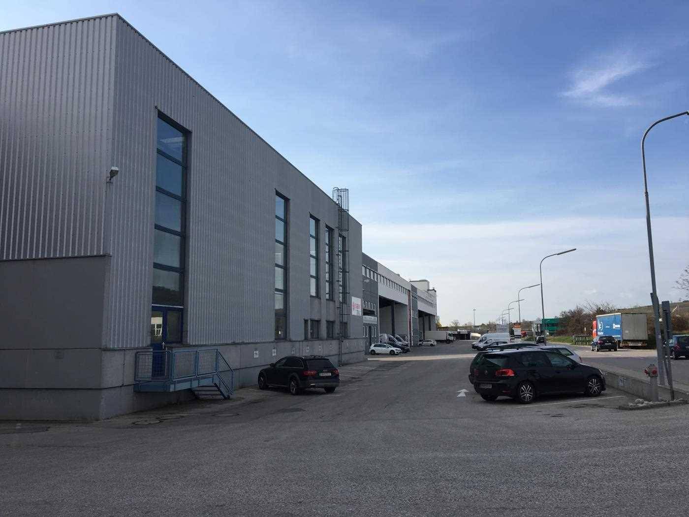 Großes Lager- oder Industriegebäude mit Wellblechfassade und Parkplatz unter bewölktem Himmel.
