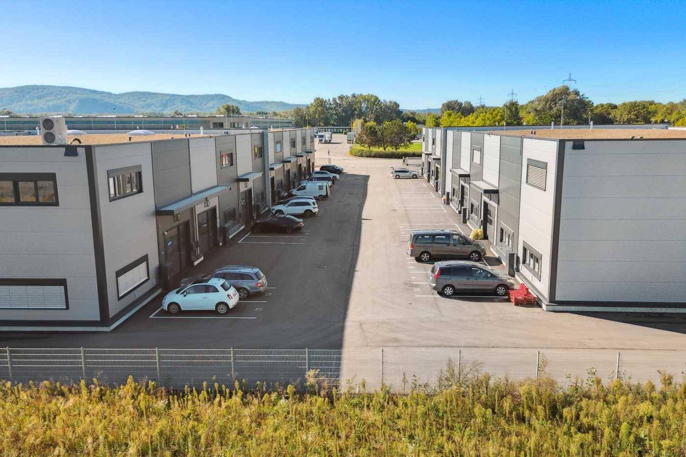 Übersicht über einen modernen Gewerbepark mit mehreren Gebäuden und Parkplätzen, umgeben von Natur und Bergen.