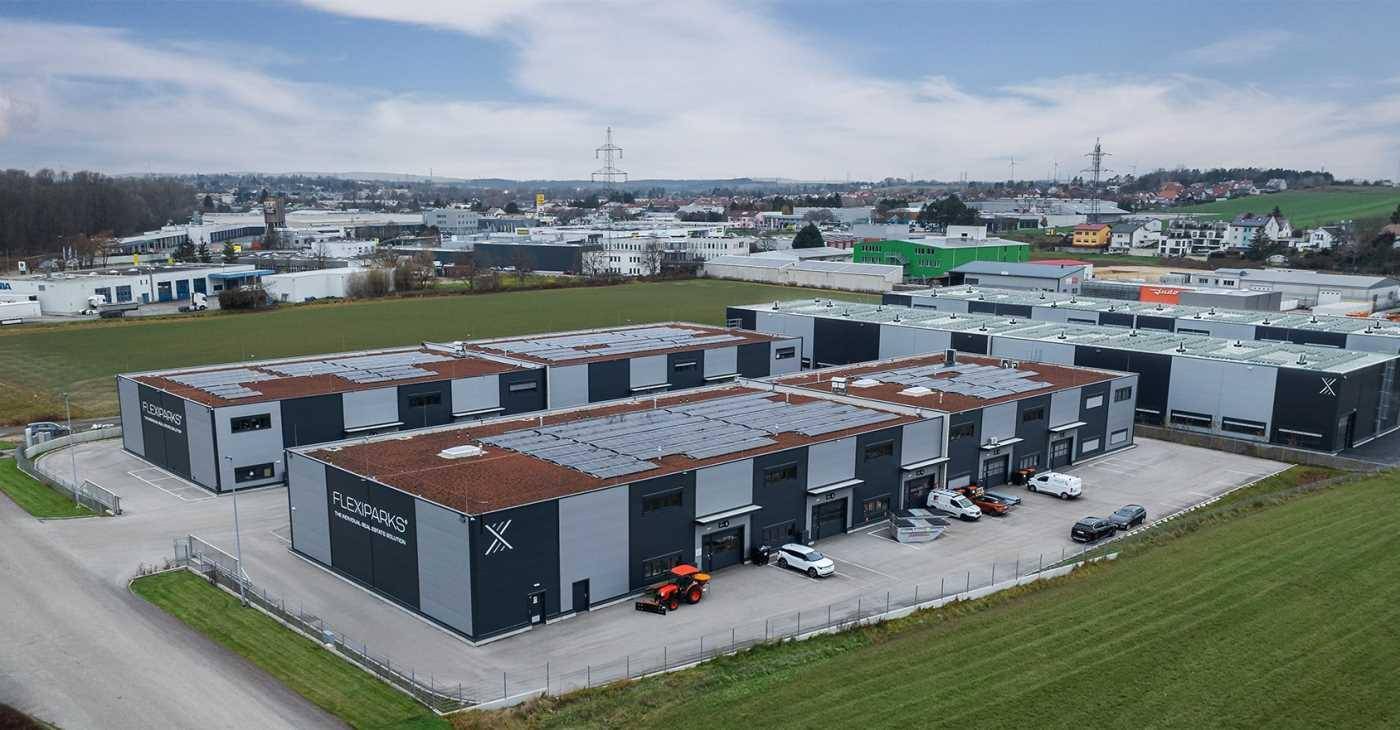 Luftaufnahme eines modernen Gewerbeparks mit mehreren Gebäuden, umgeben von Grünflächen und einer Stadtkulisse.