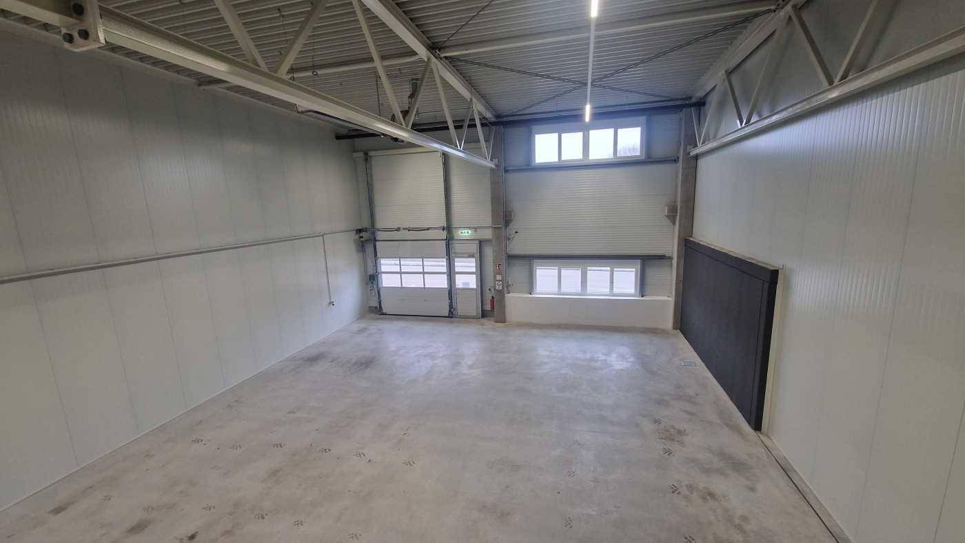 Leere Lagerhalle mit Betonboden, Rolltoren und kleinen Fenstern, bereit für die erste Nutzung.