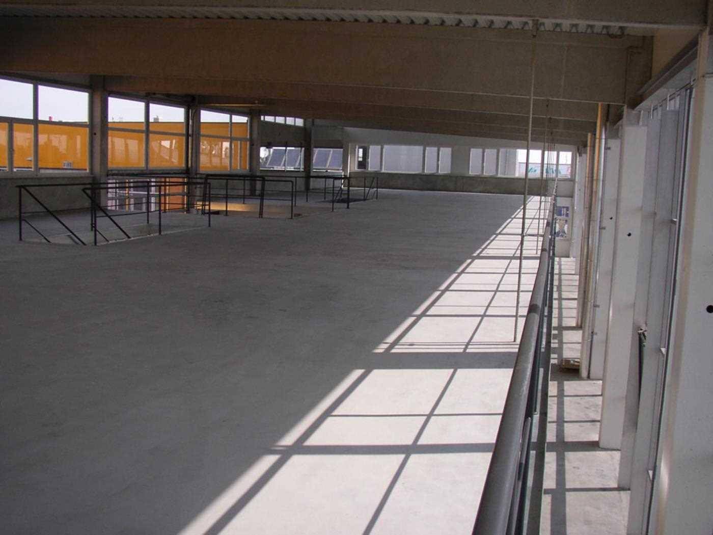 Langer, offener Gewerberaum im Obergeschoss mit Betonboden und vielen Fenstern für Tageslicht.