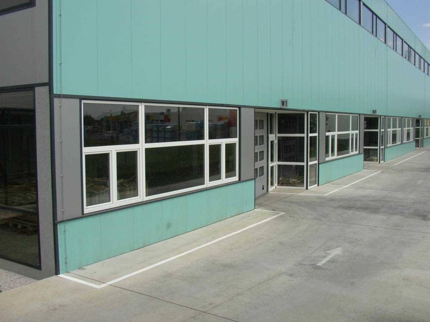 Moderne Fassade eines Gewerbegebäudes in Türkis und Grau mit großen Fenstern und Ladezonen.