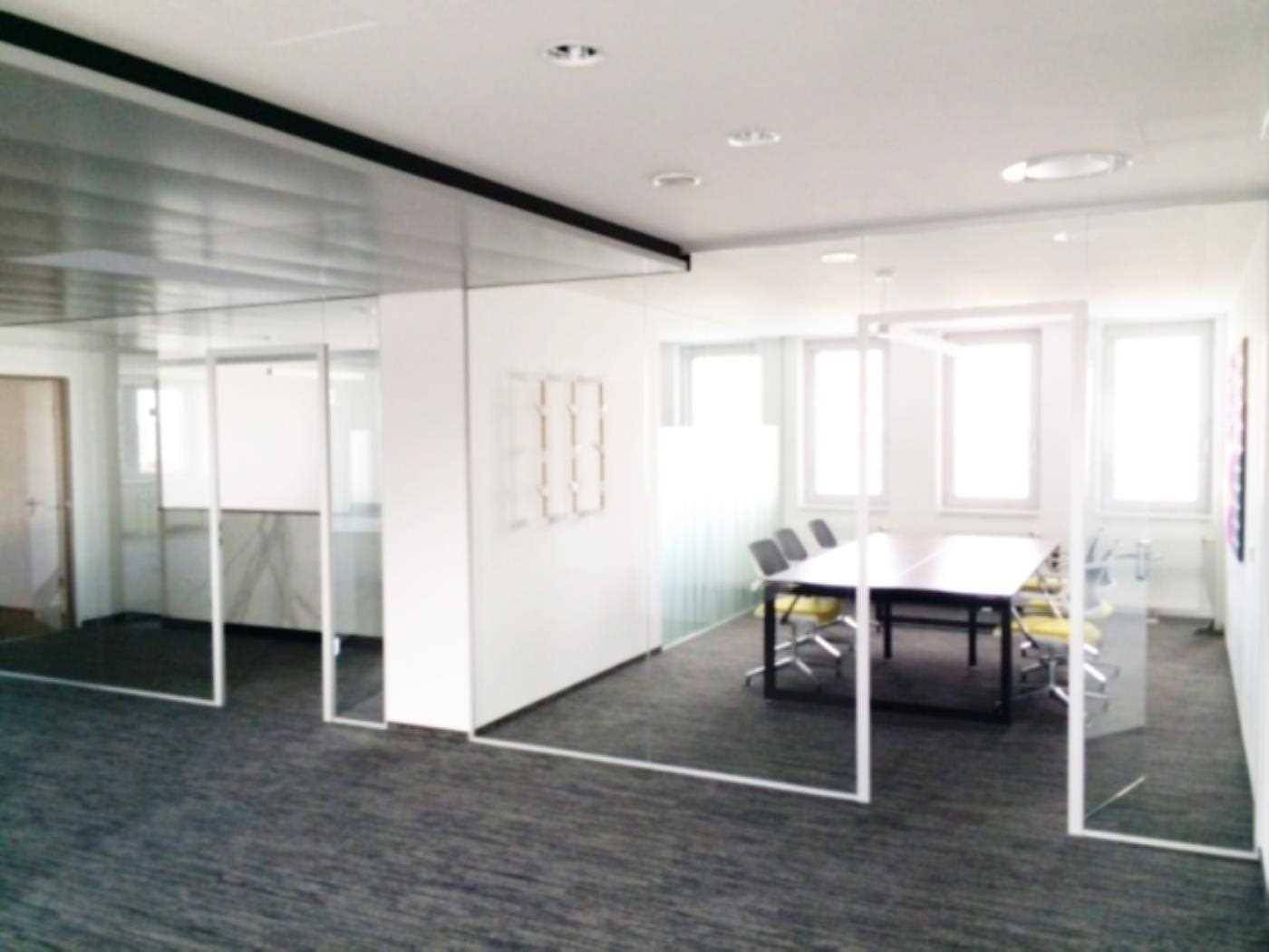 Heller Konferenzraum mit Glastrennwänden, Teppichboden und einem großen Besprechungstisch mit Stühlen.