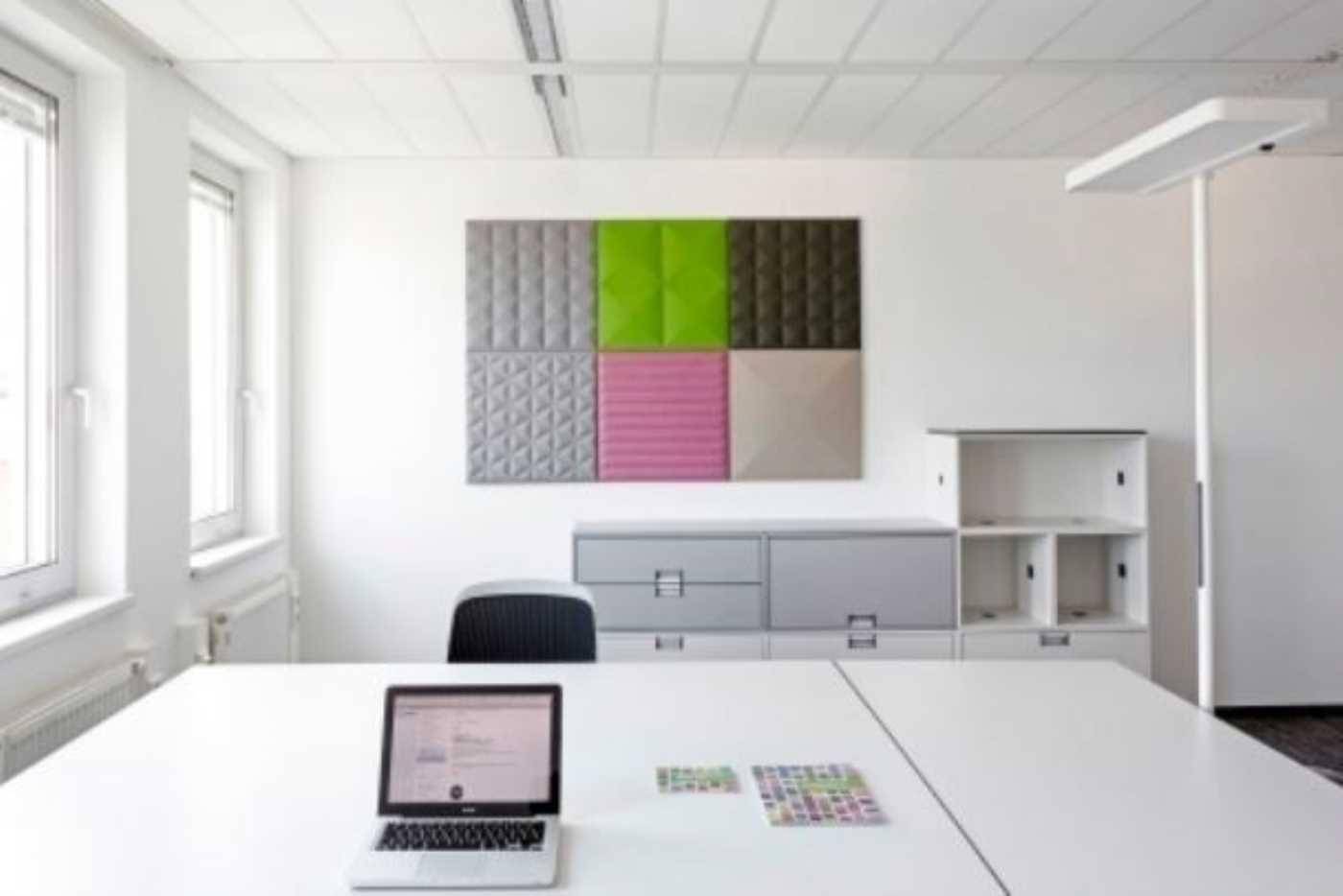 Modernes Büro mit weißem Schreibtisch, bunten Akustikpaneelen an der Wand und viel Tageslicht.