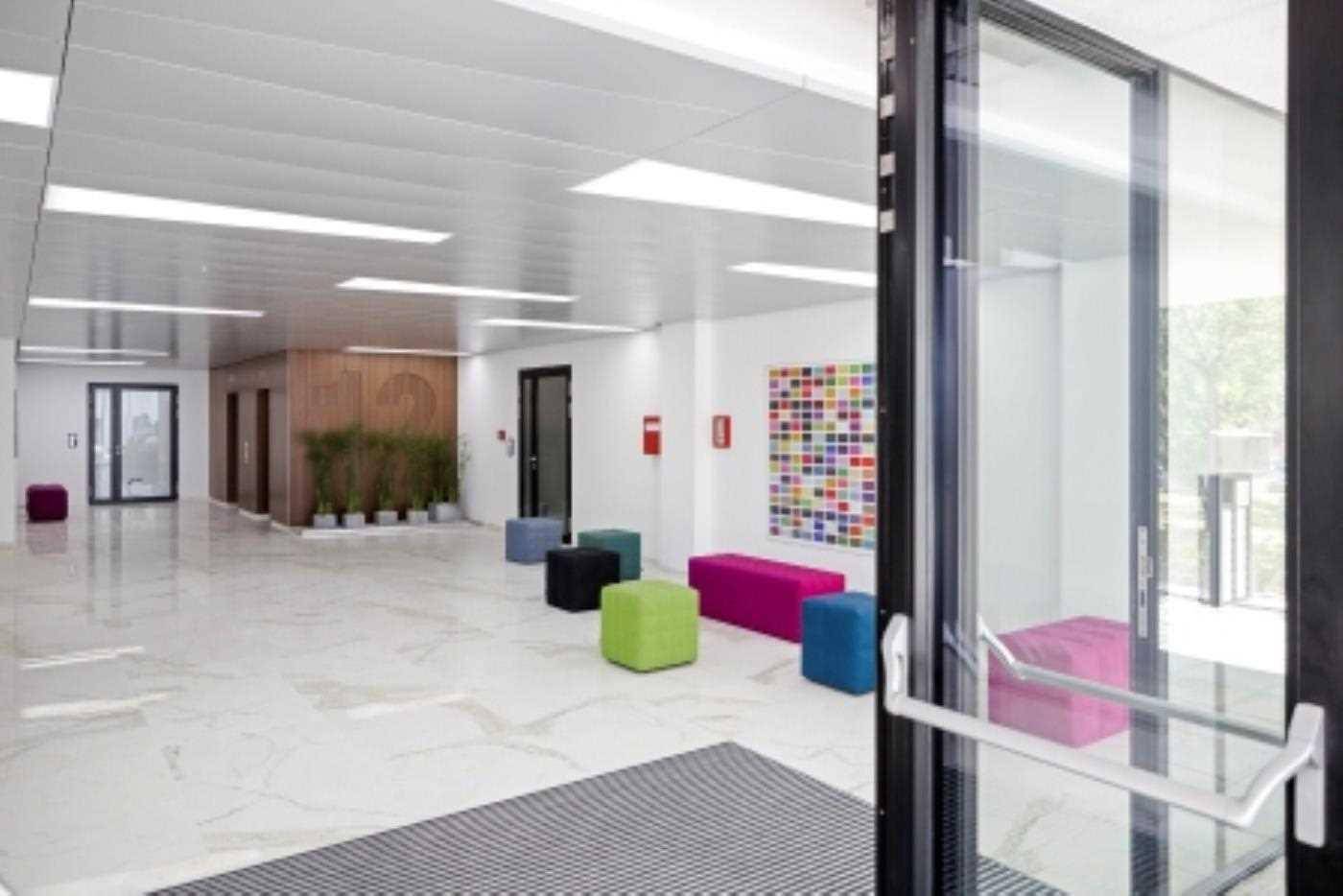 Geräumige, moderne Lobby mit glänzendem Marmorboden, bunten Sitzgelegenheiten und Aufzügen im Hintergrund.