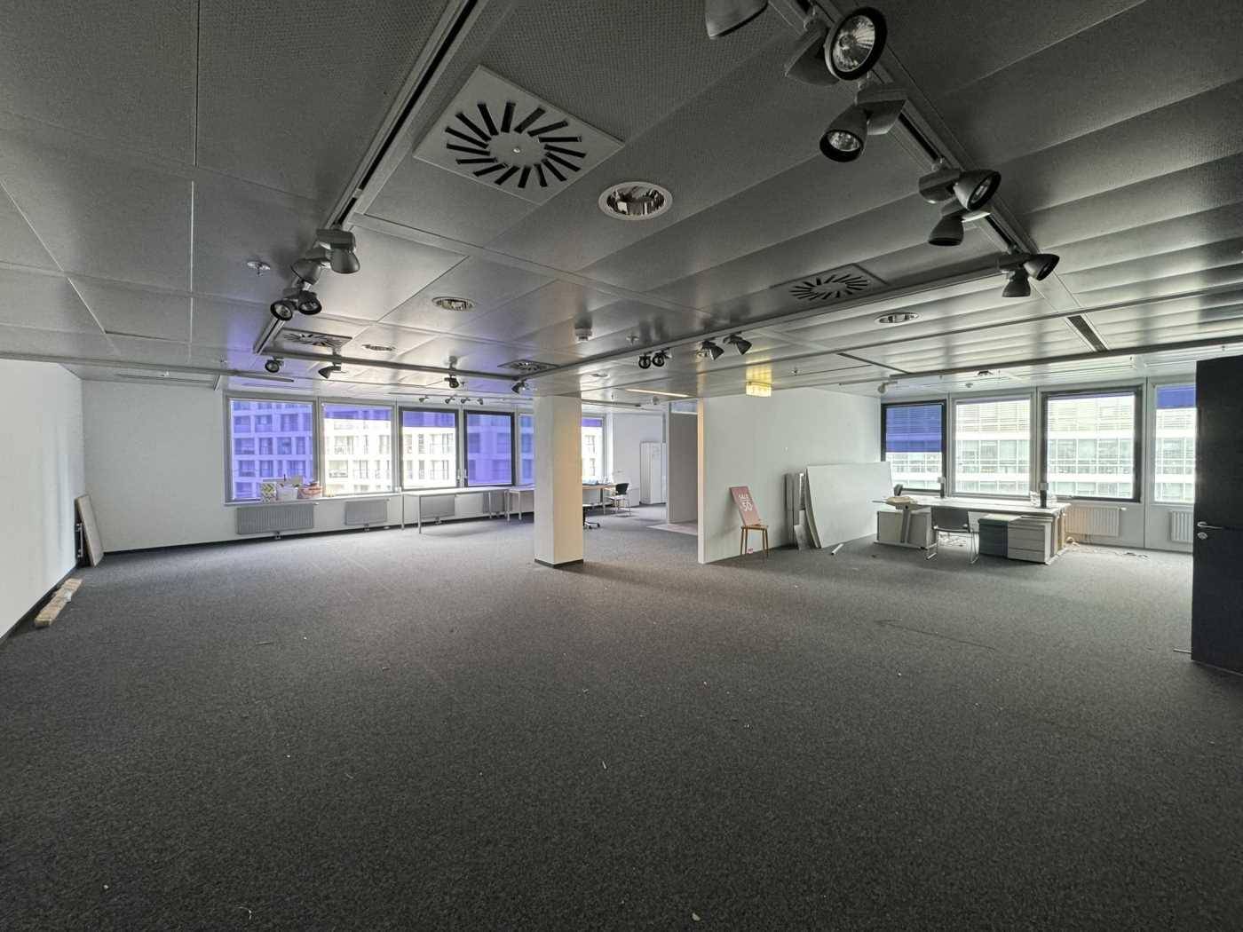 Großes, leeres Büro mit Teppichboden, abgehängter Decke und vielen Fenstern, die viel Licht hereinlassen.