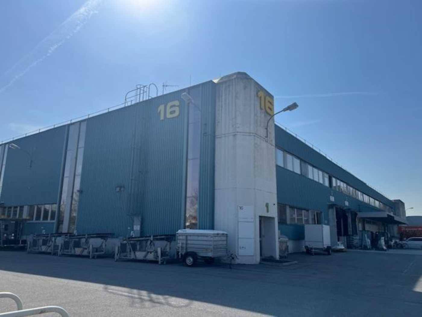 Großes Industriegebäude mit blauer Fassade und der Nummer 16, unter strahlend blauem Himmel.