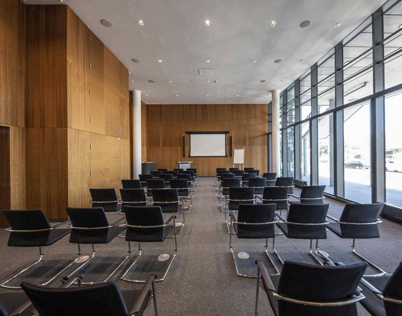 Großer Konferenzraum mit Holzvertäfelung, Teppichboden und einer Projektionsfläche, ideal für Präsentationen und Schulungen.
