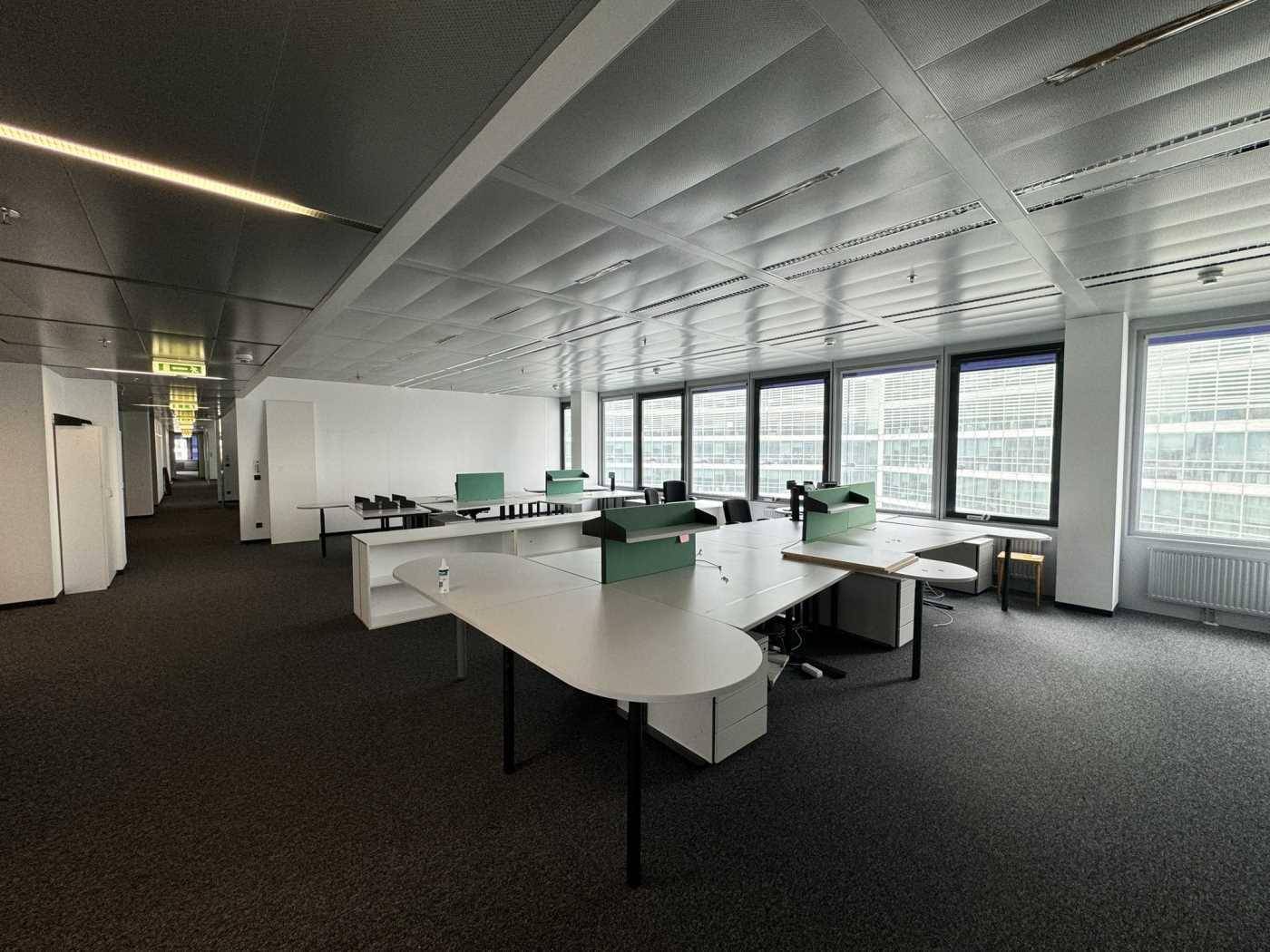Weitläufiges Büro mit Teppichboden, modernen Schreibtischen und Blick auf die umliegenden Gebäude.
