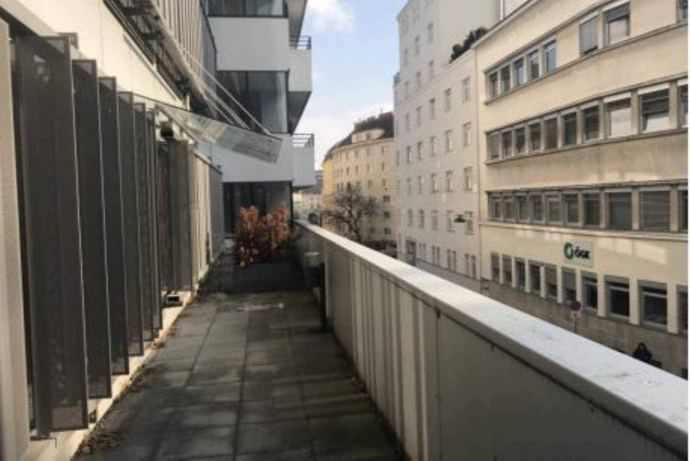 Langer Balkon mit grauen Fliesen und Blick auf die umliegenden Stadtgebäude in einer urbanen Umgebung.