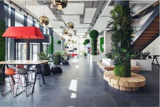 Geräumige, moderne Lobby mit hohen Decken, viel Grün und stilvollen Hängelampen.