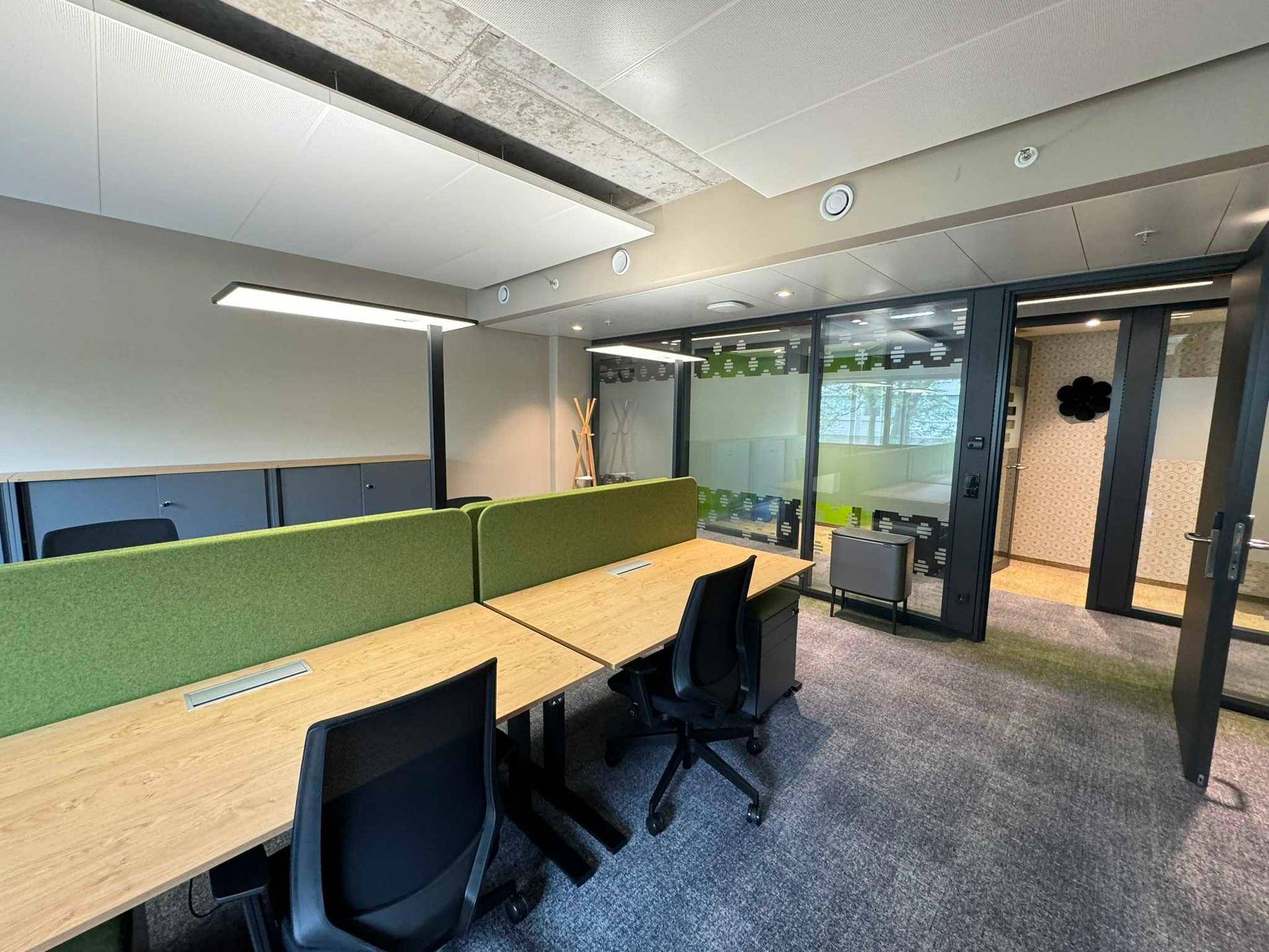Modernes Großraumbüro mit ergonomischen Arbeitsplätzen, Teppichboden und Glaswänden zu angrenzenden Räumen.