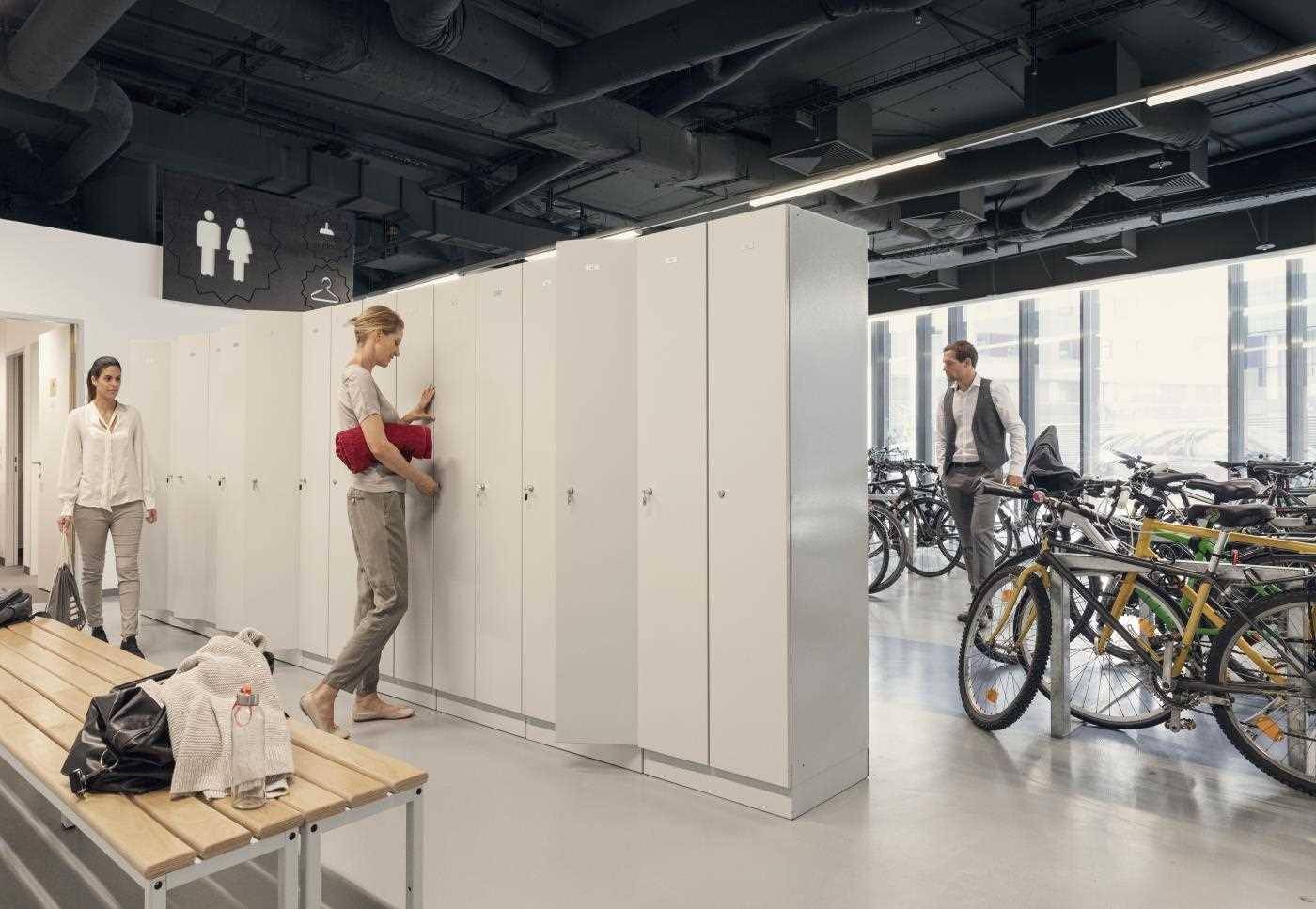 Umkleideraum mit Spinden und angrenzendem Fahrradabstellbereich in einem modernen Bürogebäude.