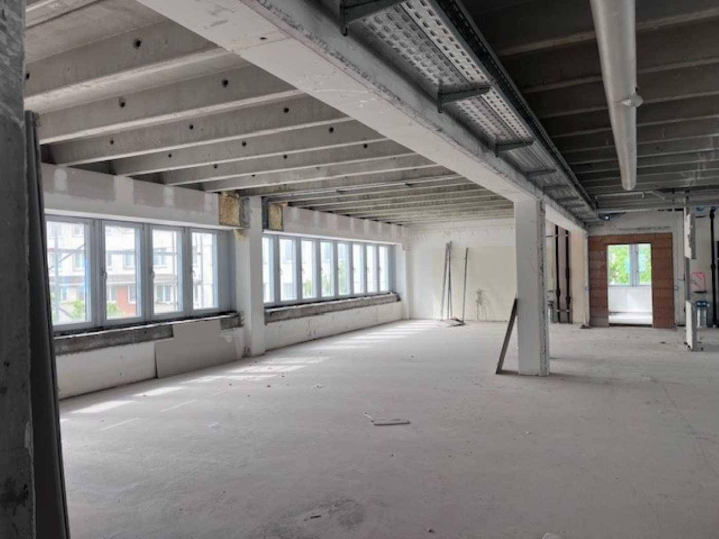 Großer, unfertiger Büroraum mit Betonwänden und -decken, vielen Fenstern und sichtbaren Installationen.
