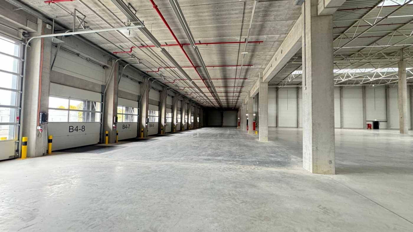 Langer Gang in einer Lagerhalle mit mehreren Rolltoren und Betonboden, bereit zur Nutzung.