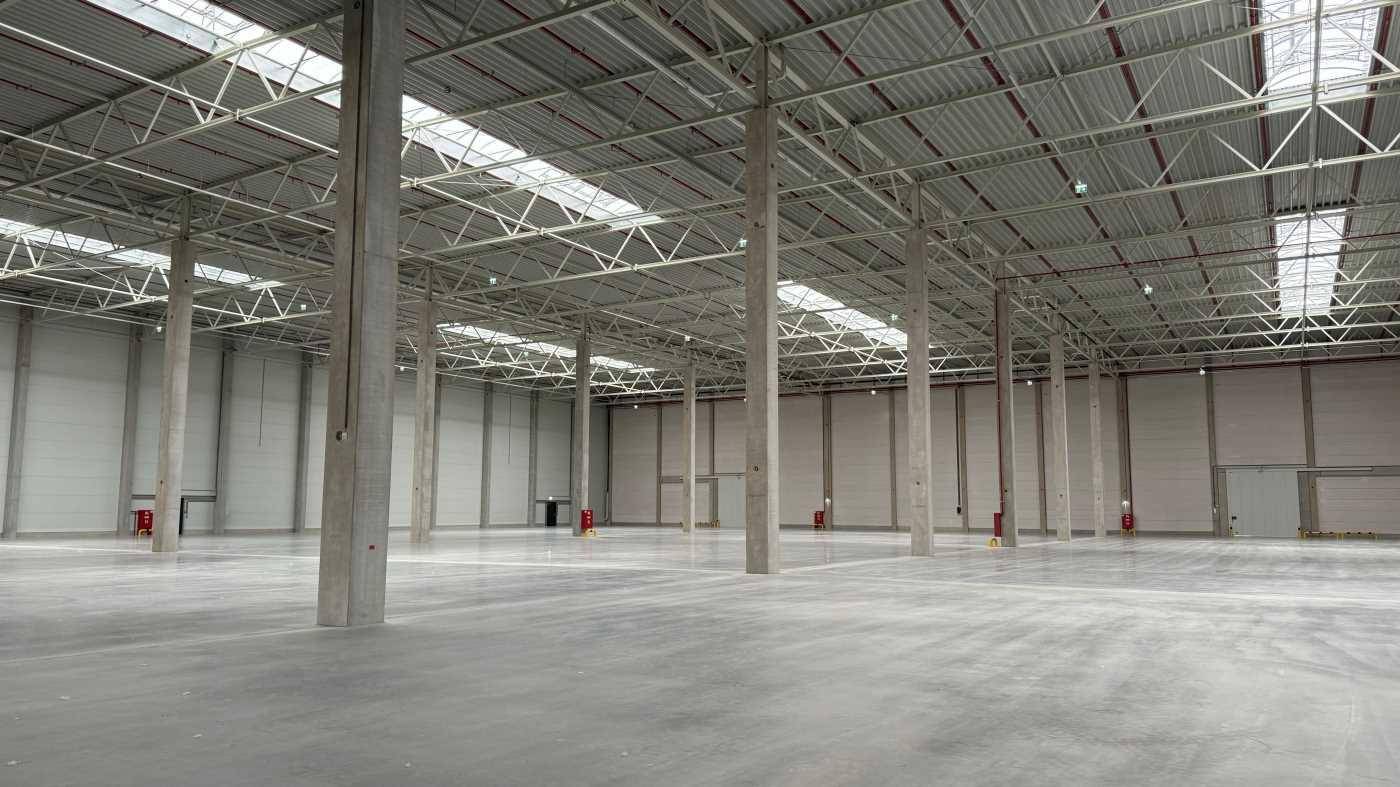 Geräumige Lagerhalle mit hoher Decke, Betonstützen und Oberlichtern für natürliches Licht.